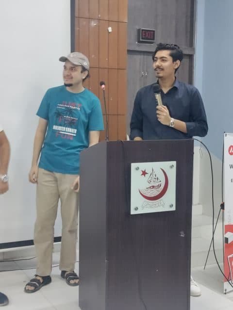 Muzammil holding the mic at the podium at the Avalanche event at Karachi University, next to another speaker.