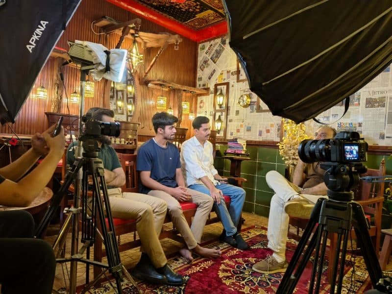 A podcast set with cameras and softbox lights, Muzammil among the guests.